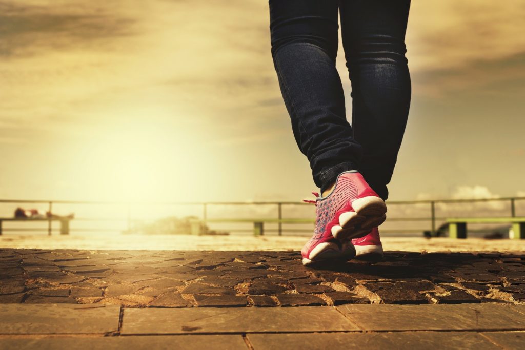 person in tennis shoes standing at a pier over looking sunrise